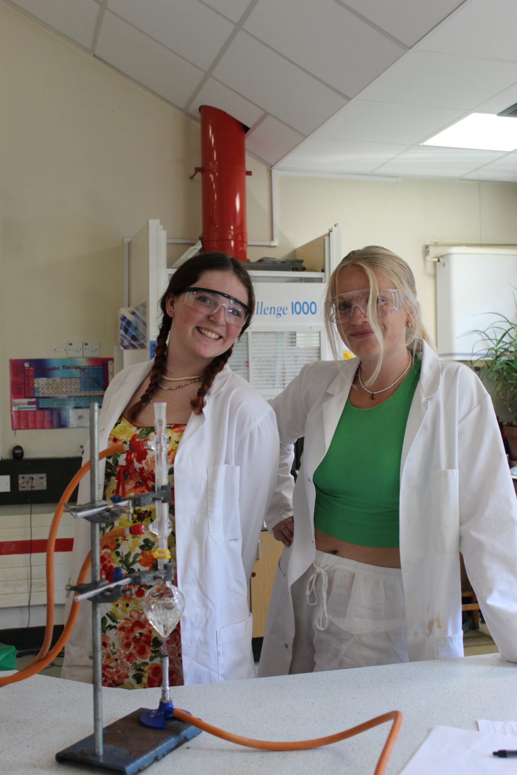 Two Gillingham School Sixth Form students in the science lab wearing lab coats and protective goggles whilst working on a science experiment.